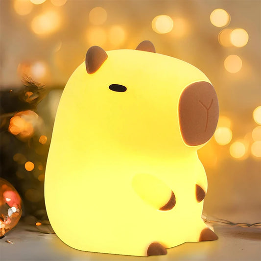 LIVSY capybara night light glowing warmly with soft yellow light against blurred warm bokeh background