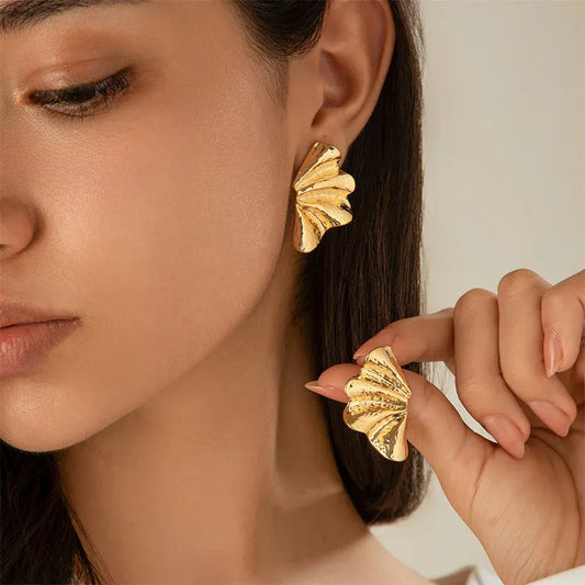Gold tone maple leaf stud earrings worn and held by a woman showcasing textured design