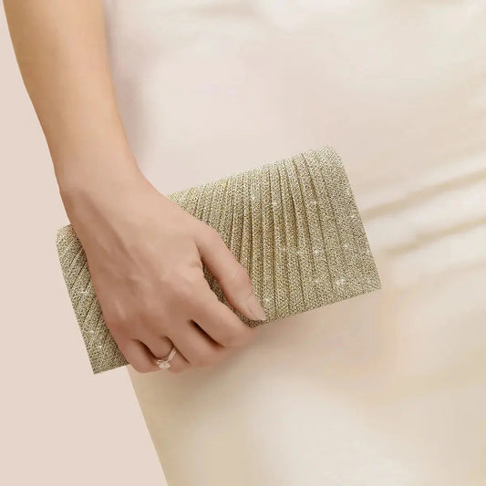 Elegant silver evening clutch purse with textured design held by hand over cream dress