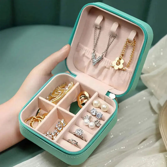 Compact travel jewelry organizer case in teal with multiple compartments holding rings, earrings, and necklaces
