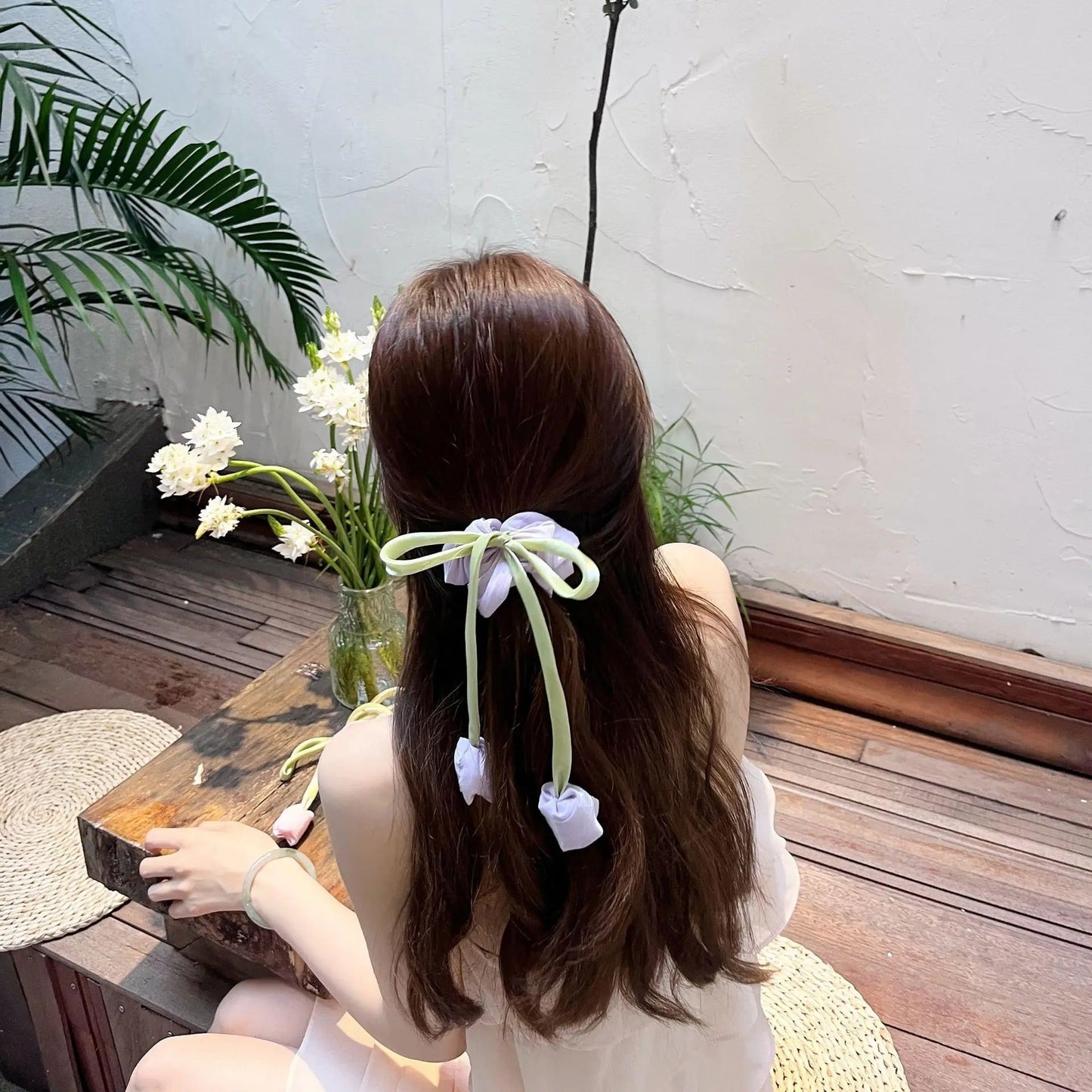 Woman with long brown hair wearing Korean style satin scrunchies tied in a bow with flower accents